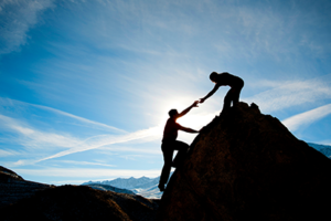 Two peope climbing mountain; hands are almost clasped as one helps the other up; managing movement