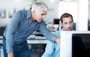 Manager telling his colleague what needs to be done on his computer screen