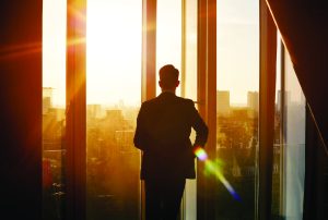 Man looking out office window at sunset