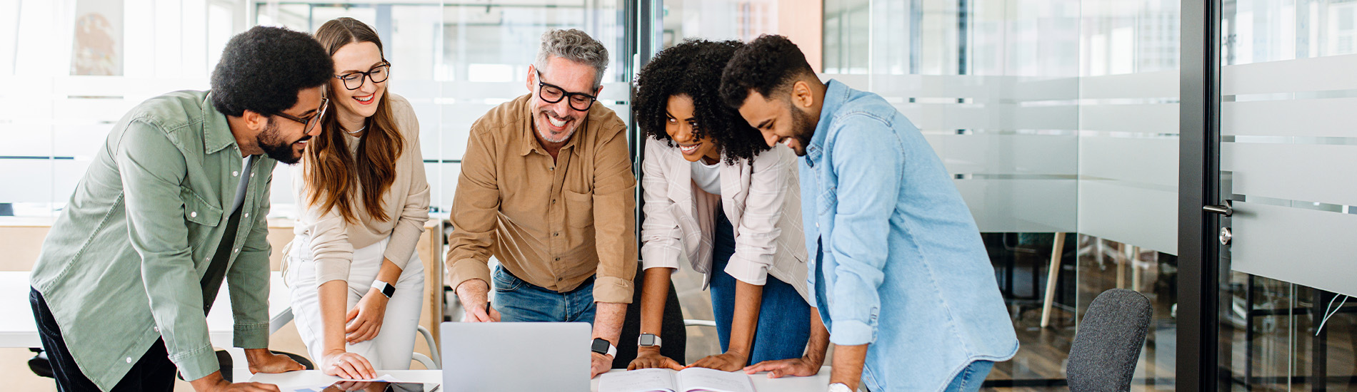 A group of coworkers huddling around a laptop and smiling.
