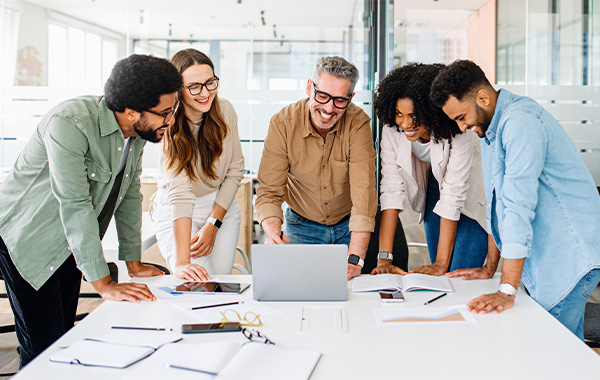 A group of coworkers huddling around a laptop and smiling.