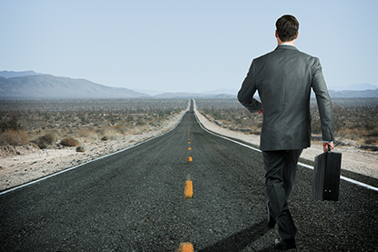 Businessman in suit; walking down desert road holding a black briefcase