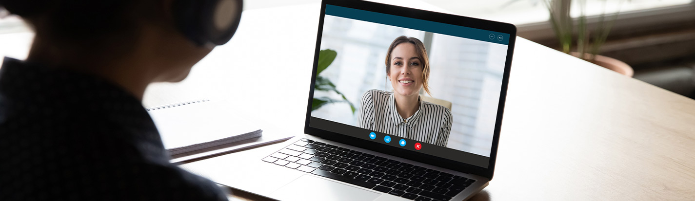 Back view of female employee sit at desk at home have Webcam conference on laptop with business partner or client, woman worker talk on video call with coworker or consultant, watch online webinar