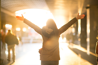 Orange washed image of girl facing away with hands triumphantly in air