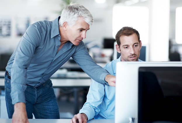 Manager telling his colleague what needs to be done on his computer screen