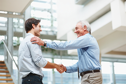 two male professionals shaking hands in agreement; both men smiling