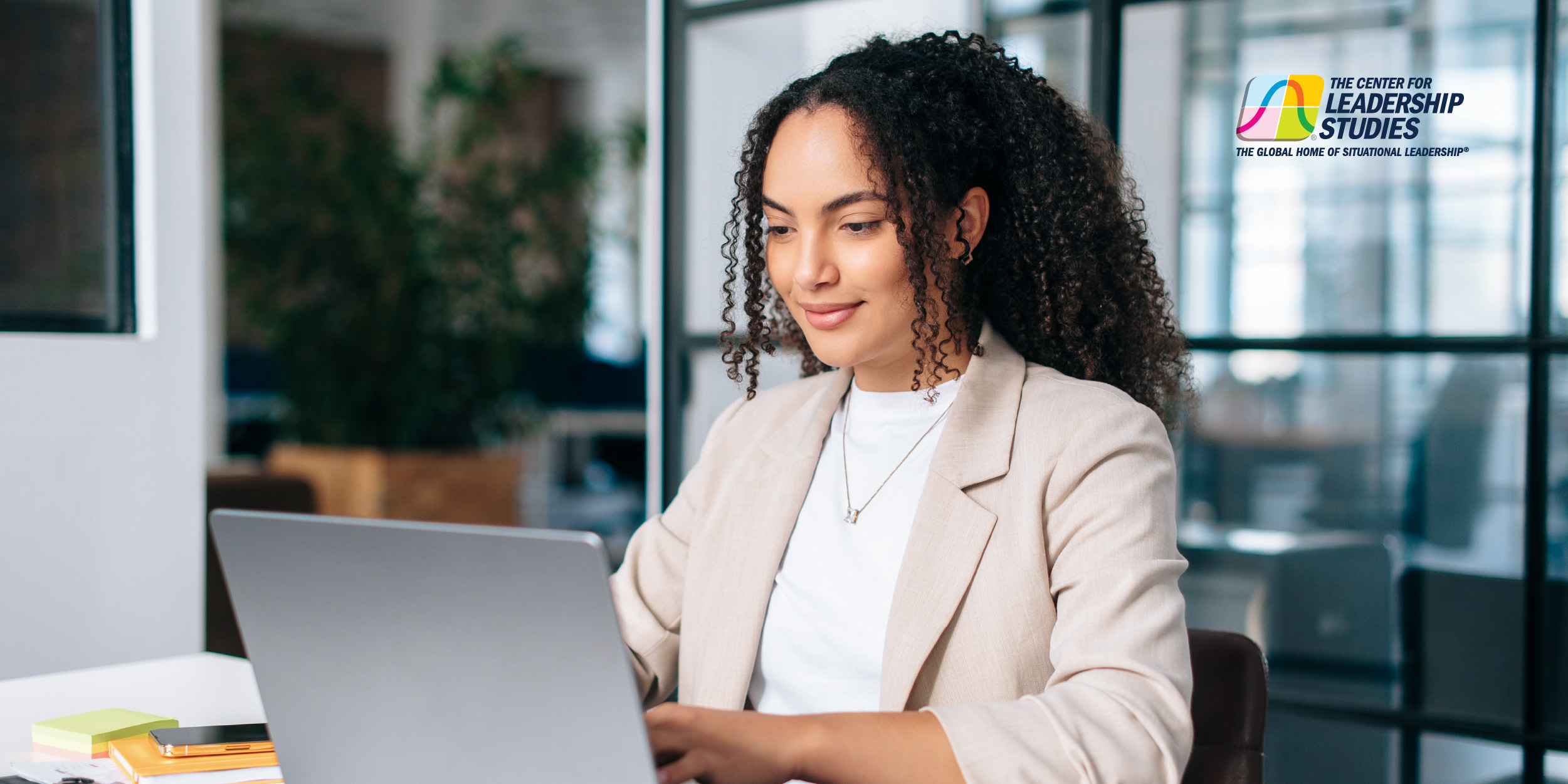 A working professional in a cream blazer typing on a computer