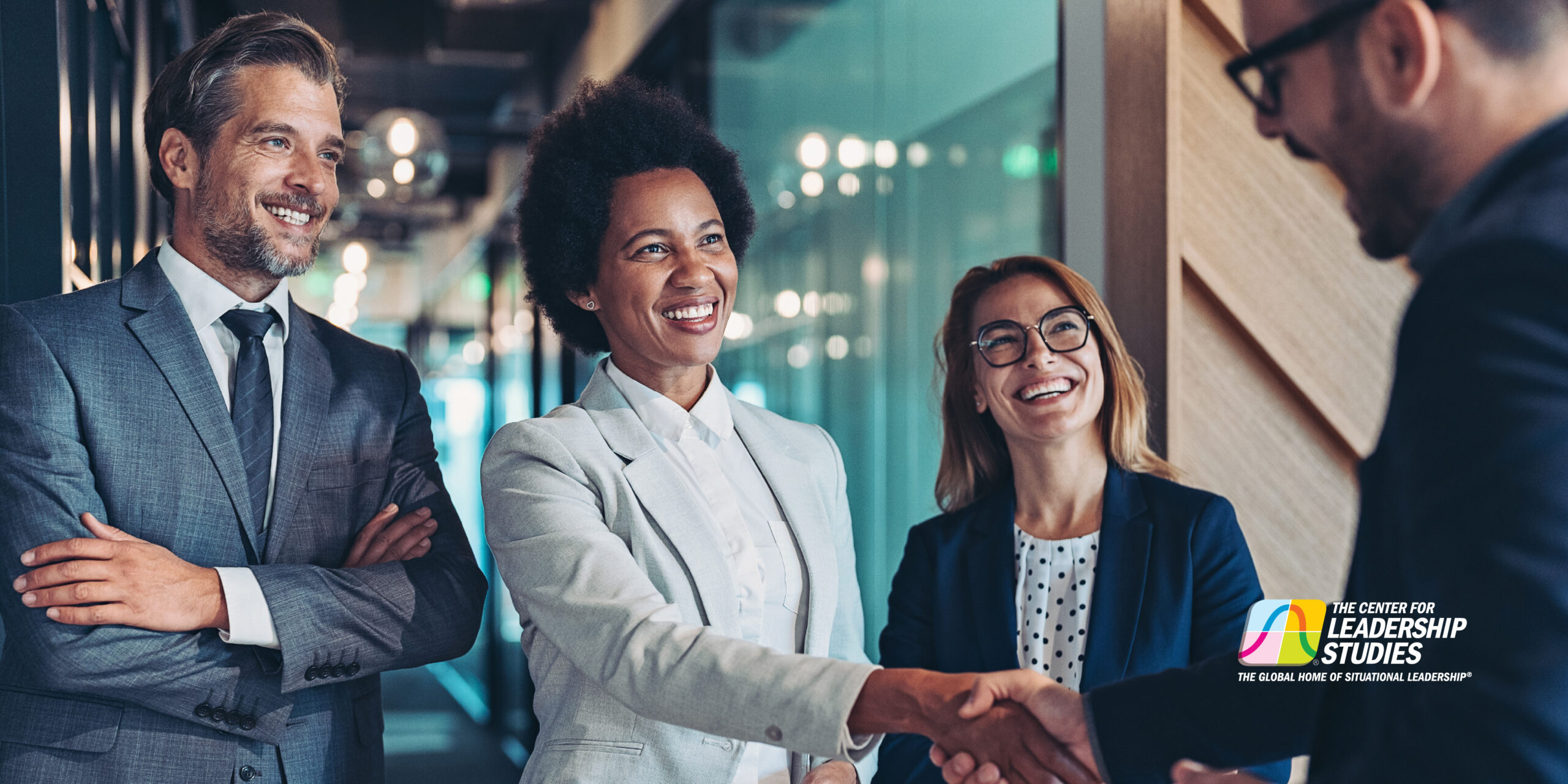 In a group setting, a woman in a suit shakes hands with a colleague.
