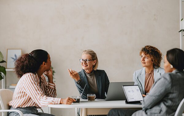 Colleagues gathered around a leader who is speaking at the center of the table.