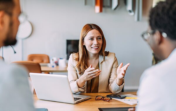 A leader speaking to two employees across a desk.